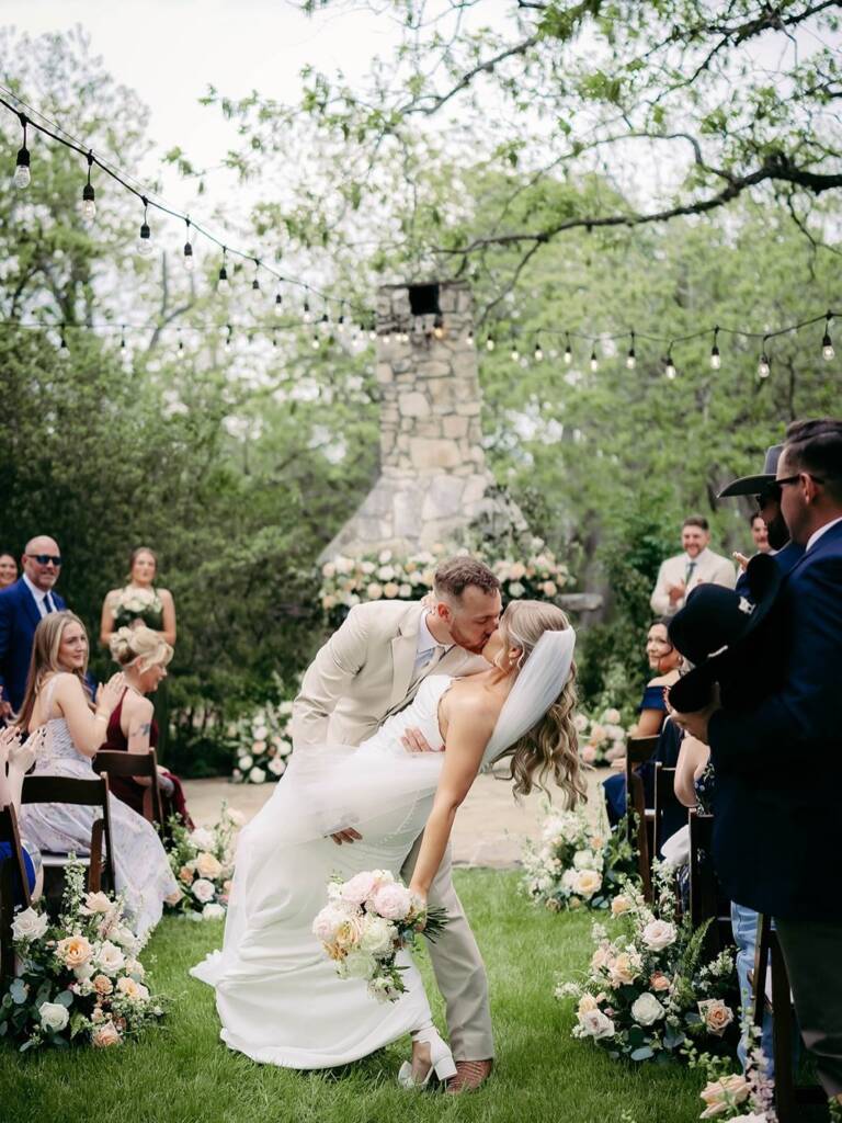 A rustic stone fireplace wrapped in lush greenery, string lights, and peach-and-white blooms set the dreamiest backdrop for Megan &